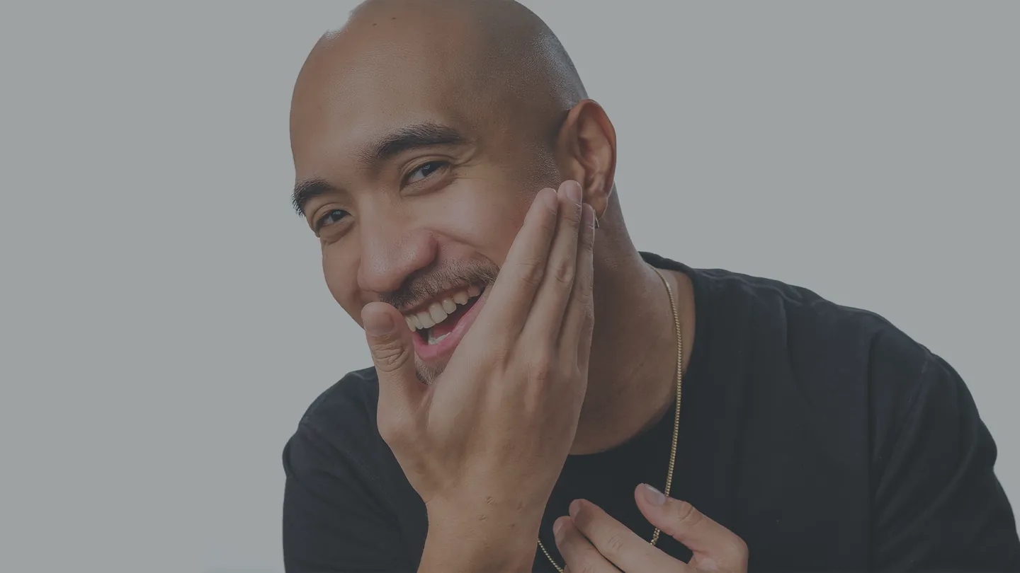 Man with a bald head smiling with his hand on his face against a gray background