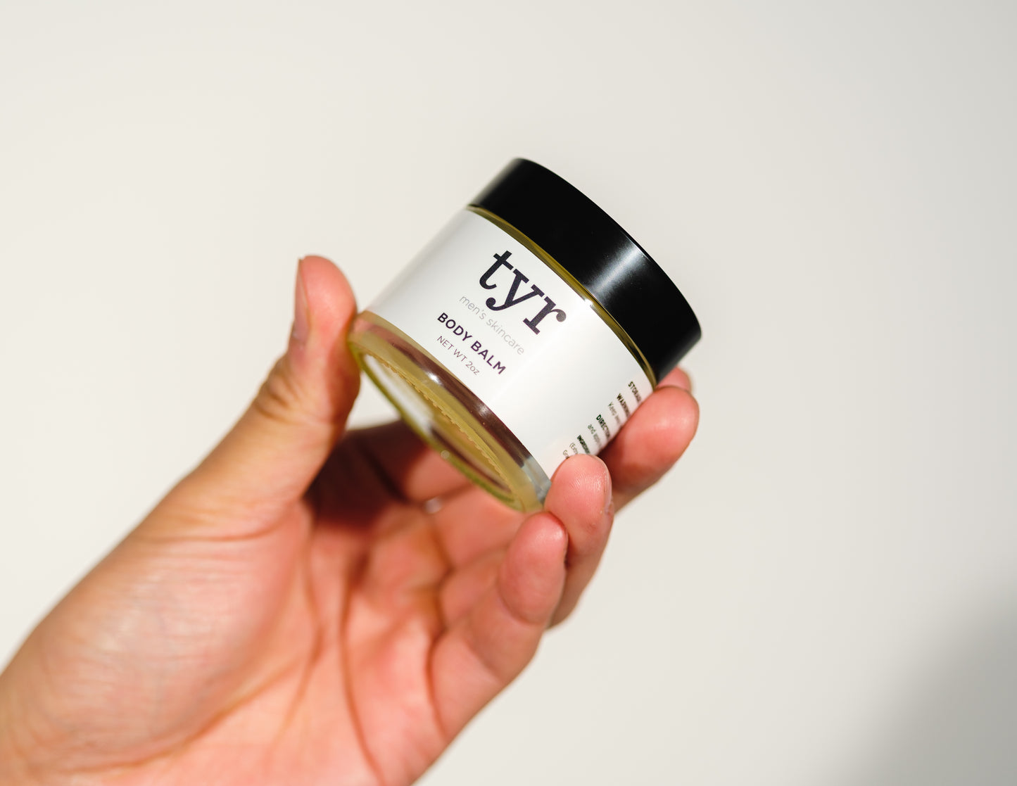 Body Balm Isolated in white background being held up by male hand, straight on angle