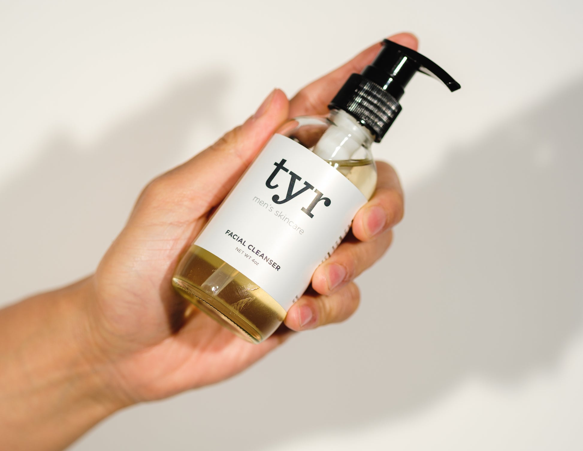 Tyr Skincare for men isolated in white background and held up by hand, angle straight on